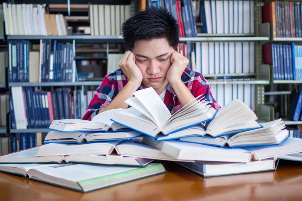 man looking overwhelmed behind a pile of open books